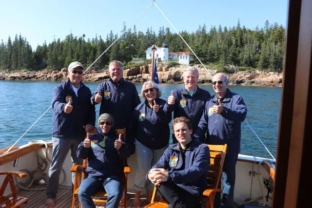 ALPS advisors in matching navy jackets giving thumbs up on a boat off a Maine lighthouse