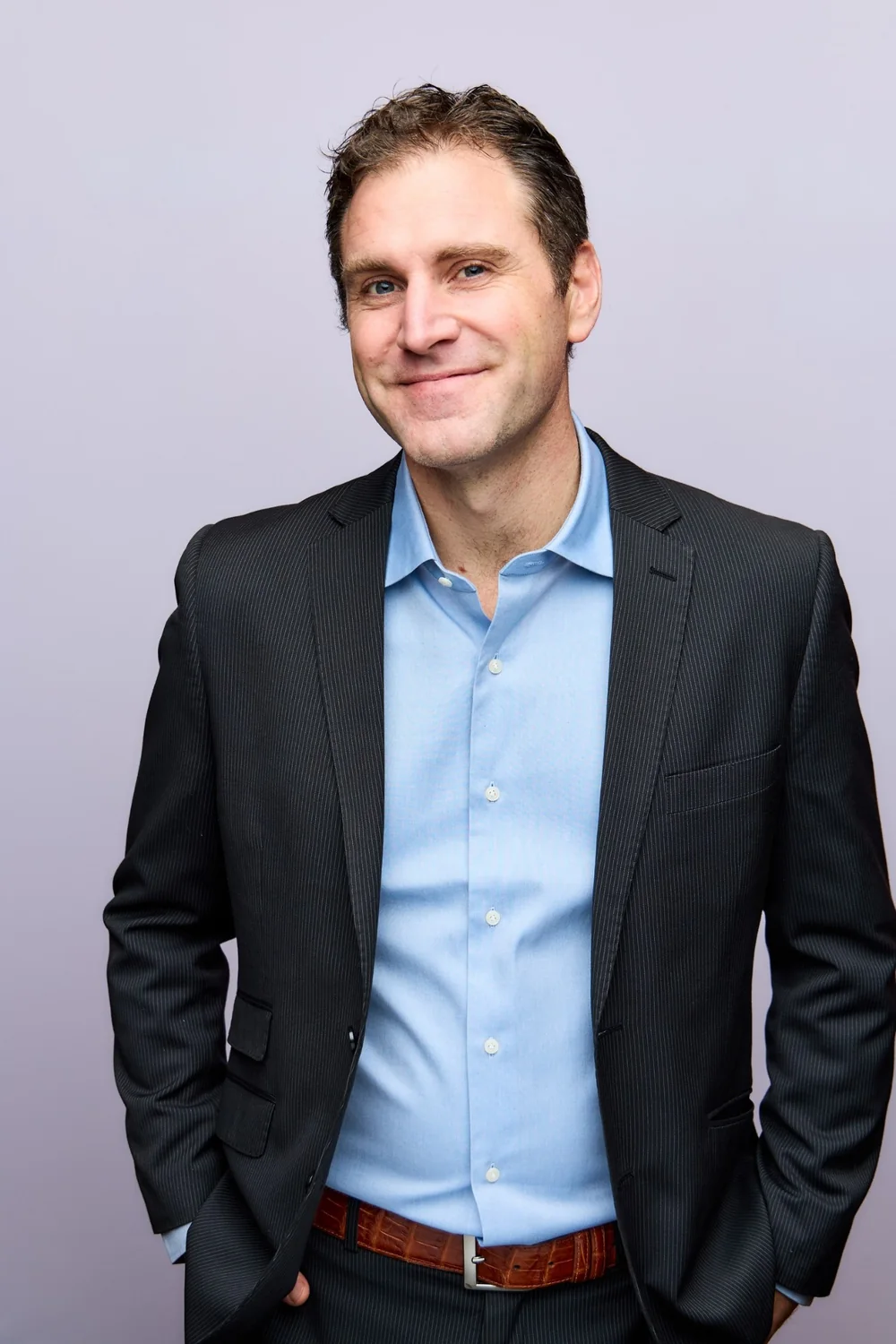 Sam Peret, smiling, hands in pockets, in a dark pinstripe suit and open blue shirt