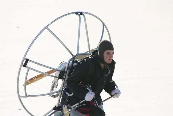 Strapped into a paramotor on the snow, propeller cage behind, about to take off