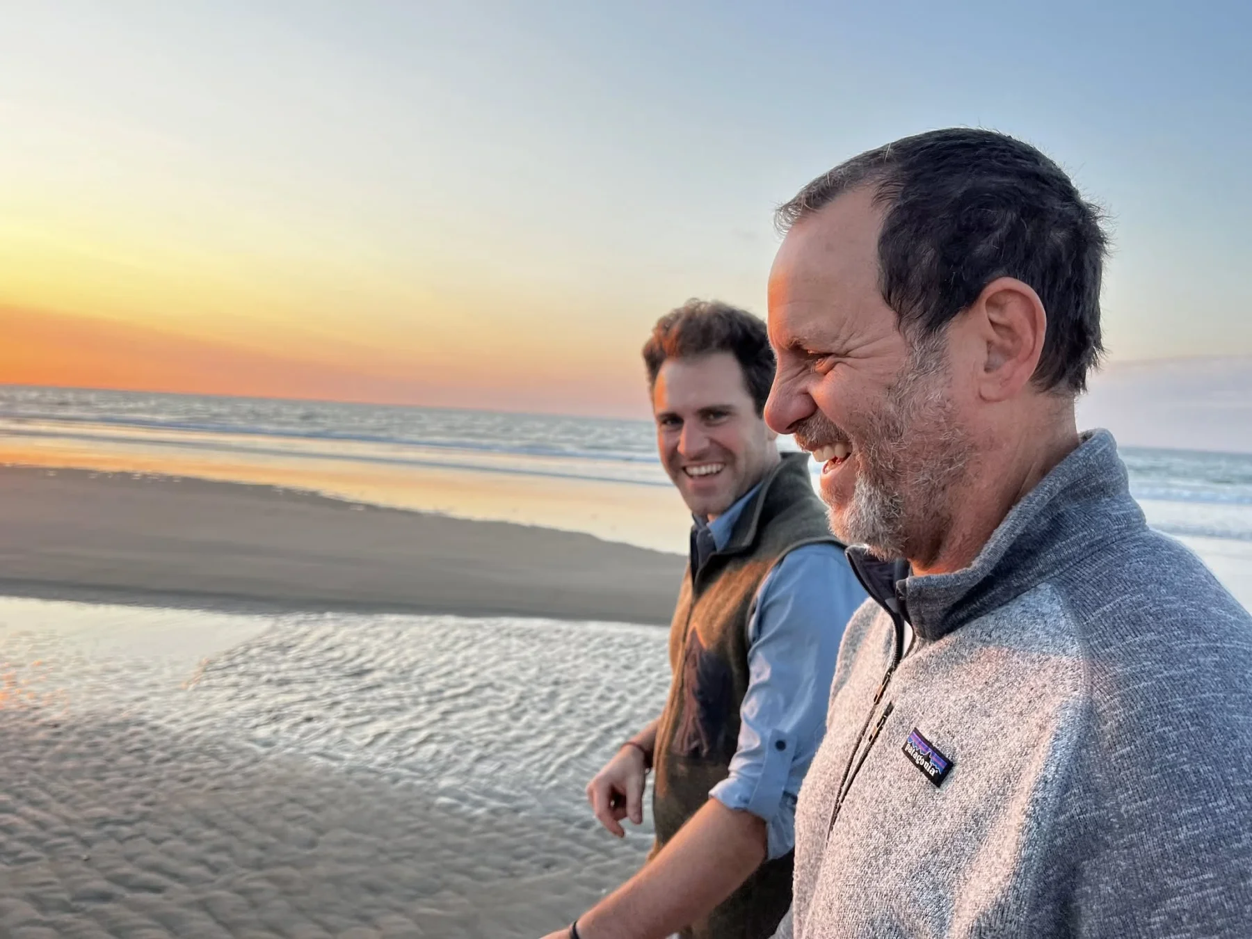 Laughing with two friends on a wide beach at sunset, the tide out