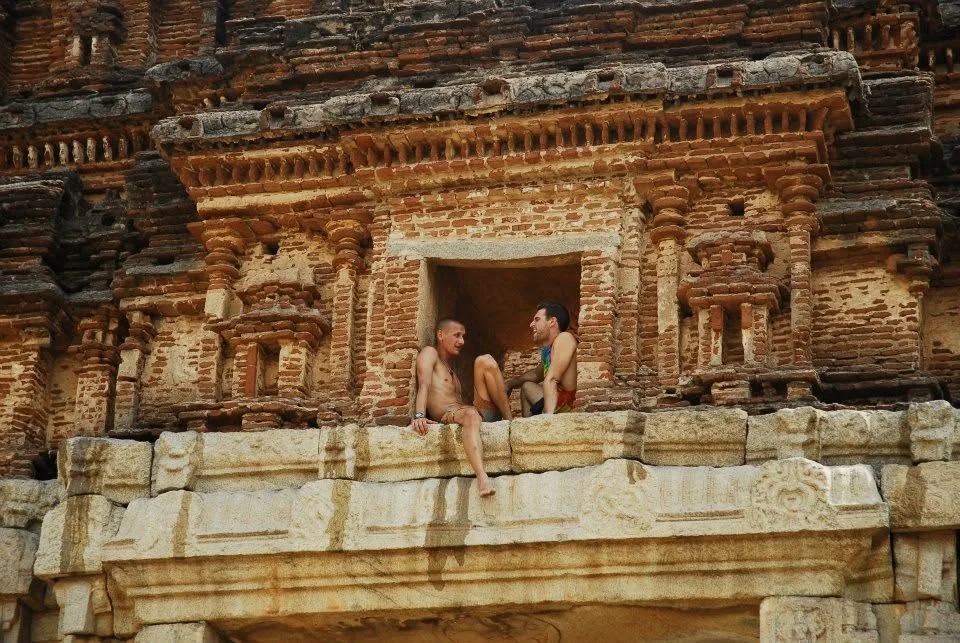 Two friends sitting in a niche of a carved stone temple façade in India